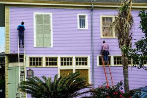 Painters on ladders in front of purple building